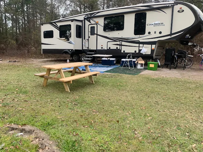 A fifth wheel parked on a grassy site at Tiny Woods, with a wooden picnic table in the foreground